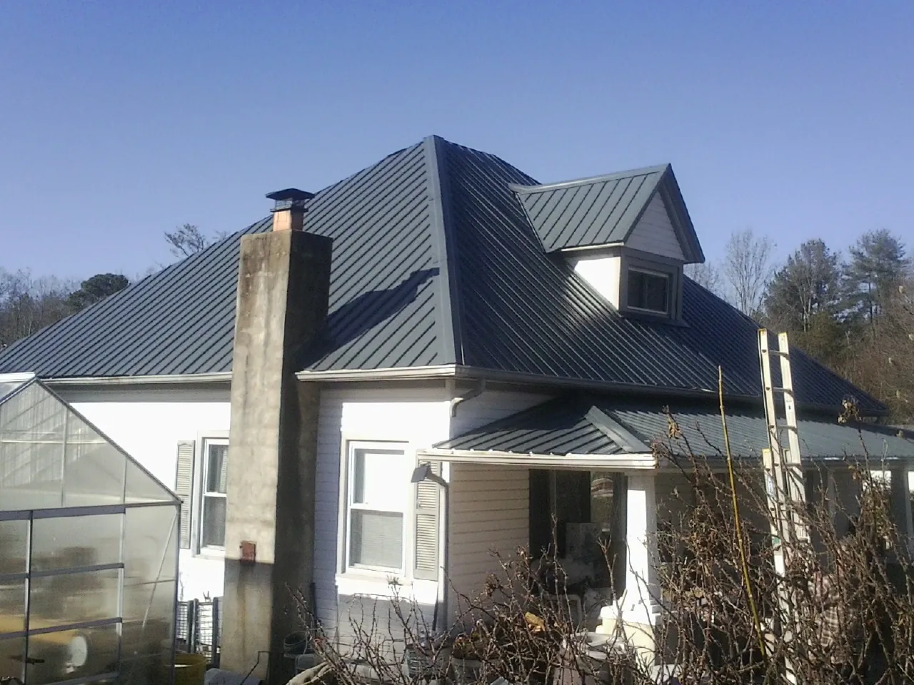 Dark blue standing seam metal roof on a white farmhouse with dormer — Slate & Tile Roof Repair by Roofing Brothers in Oklahoma City
