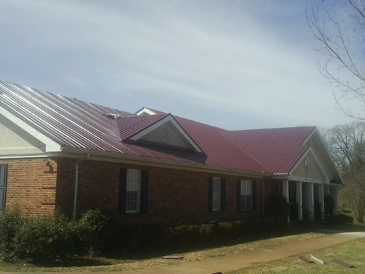Red metal roof with gabled entries on a long brick building, from a Hail Damage Roof Repair job in Oklahoma City
