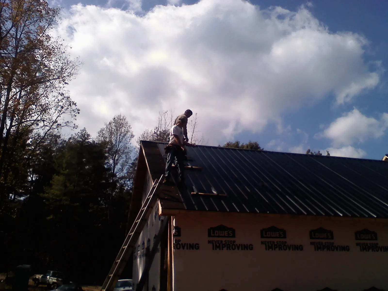 Roofer fastening dark metal panels high against a cloudy sky, from a Roof Inspection job in Oklahoma City
