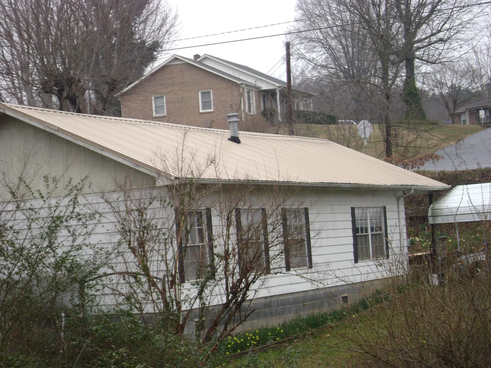Tan metal roof on a white sided house set into a hillside — Commercial Roofing by Roofing Brothers in Oklahoma City