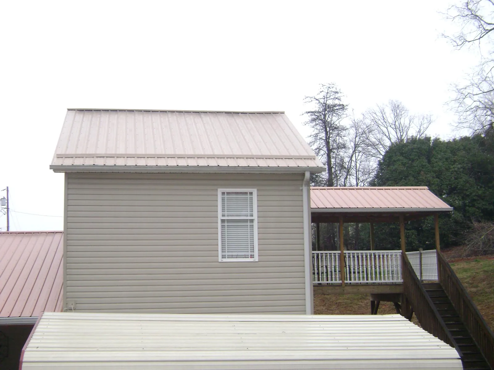 Tan metal roofs on a two story addition and attached porch, from a Roof Replacement job in Oklahoma City